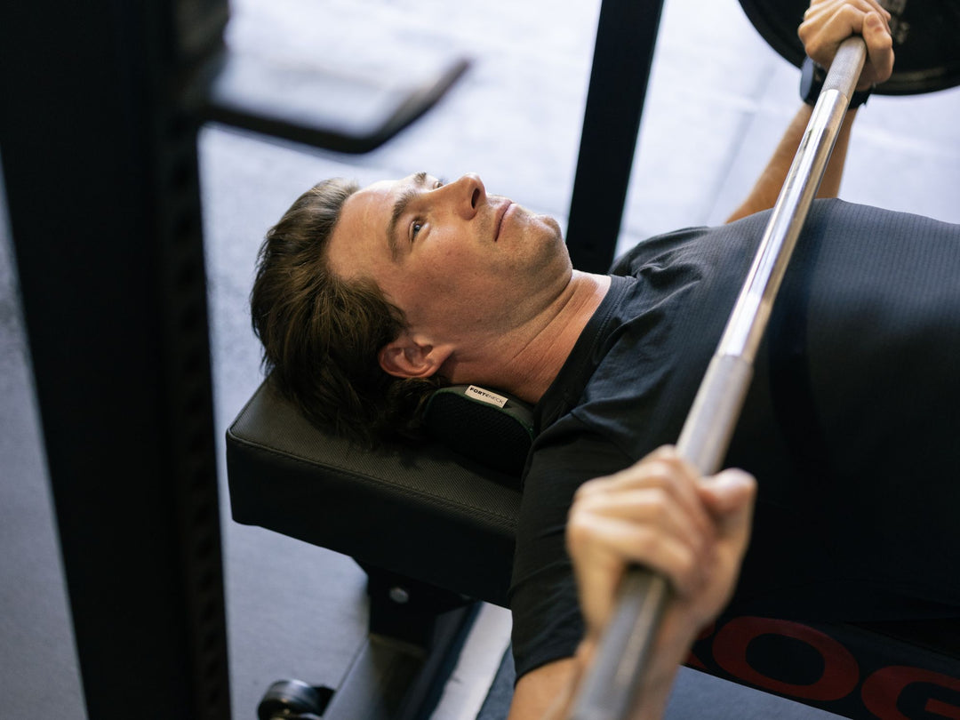 Man performing a bench press with forteneck neck cushion in a gym setting