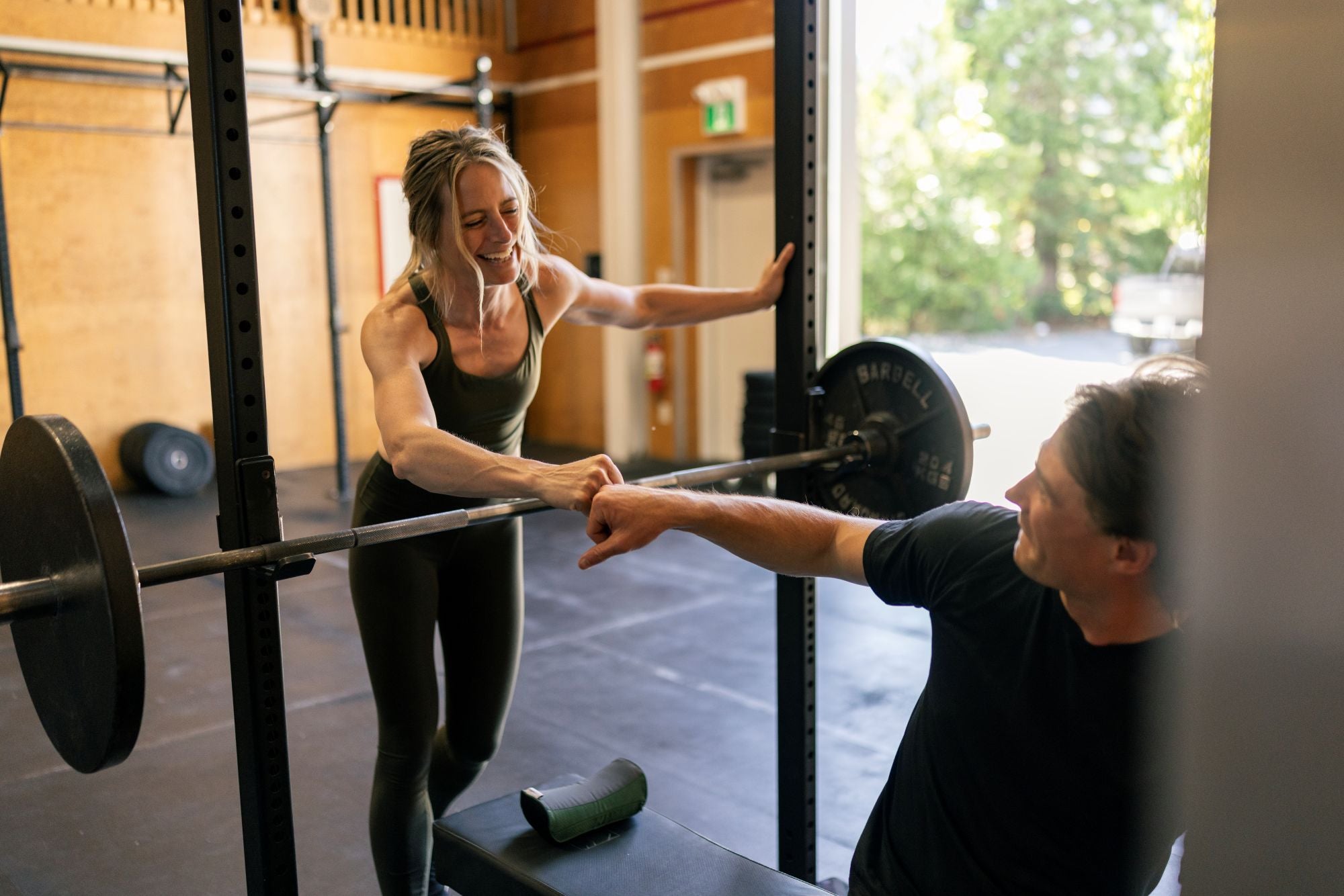 Woman fist bumping a man with a barbell in a gym setting