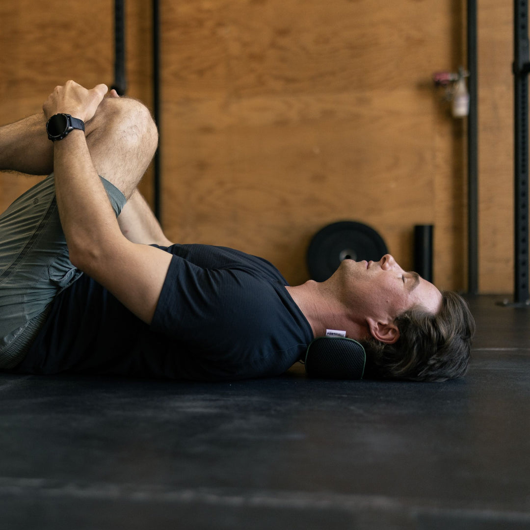 Person lying on a mat in a gym with neck resting on neck cushion and stretching legs
